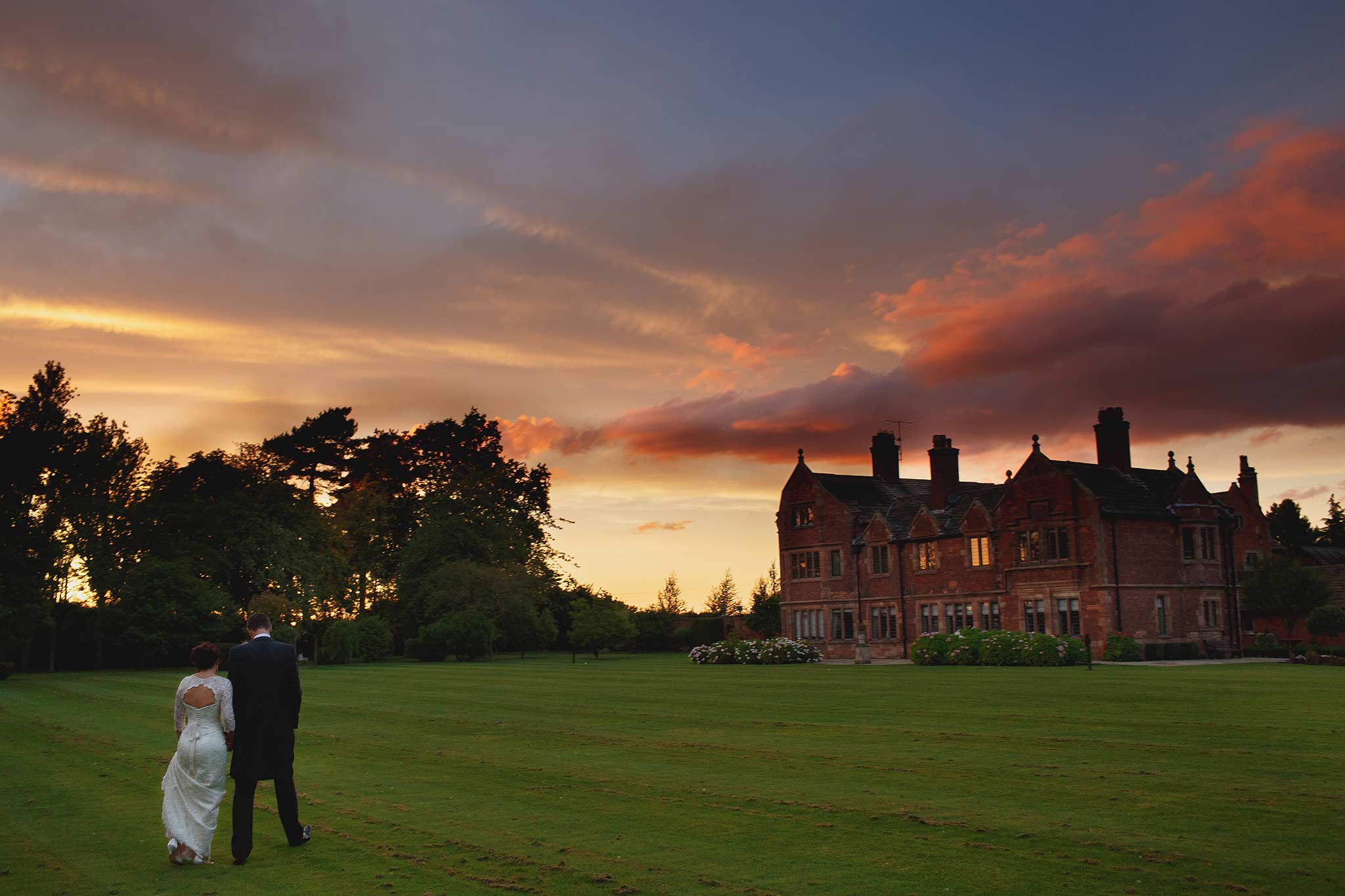 wide angle image of a bride and groom walking away at sunset at colshaw hall