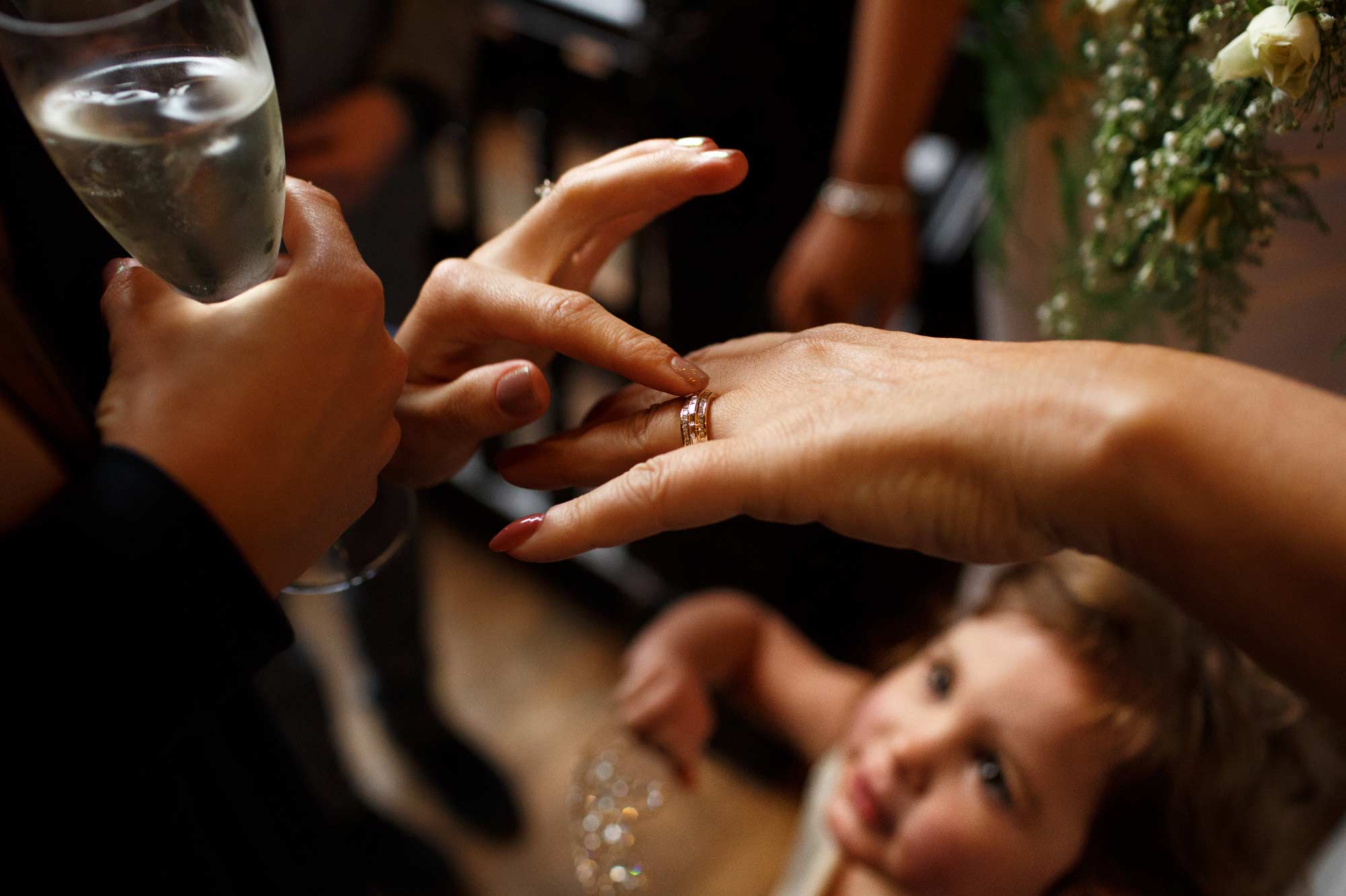 Documentary wedding photograph of bride showing guests her new ring with a girl looking up