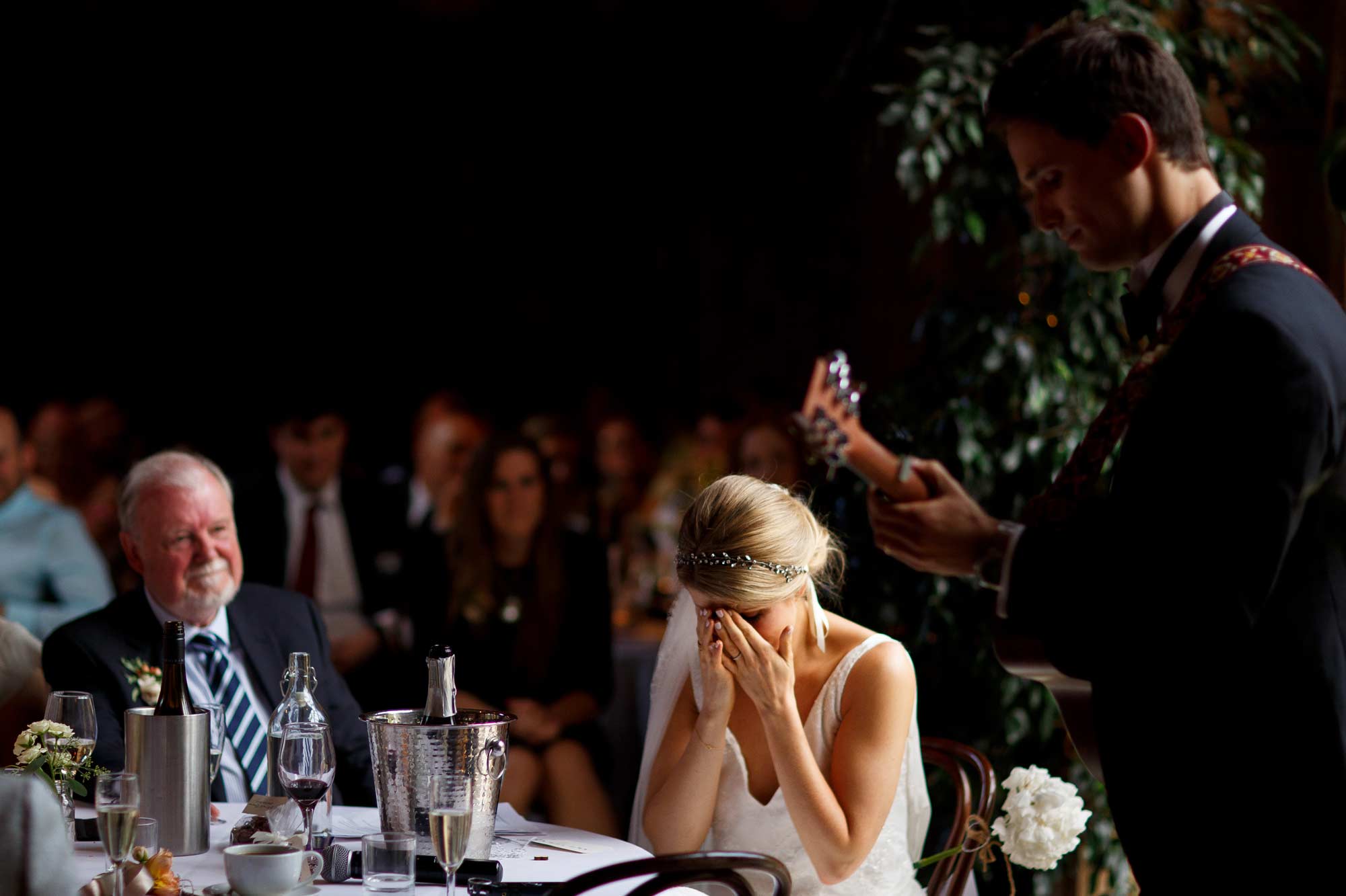 Emotional bride as her groom serenades her by playing the guitar during wedding speeches