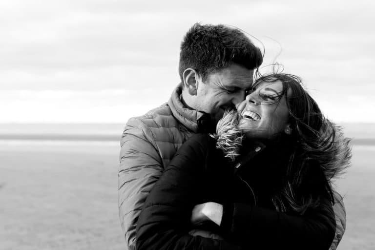 couple laughing in each others arms on the beach at sunset during engagement shoot