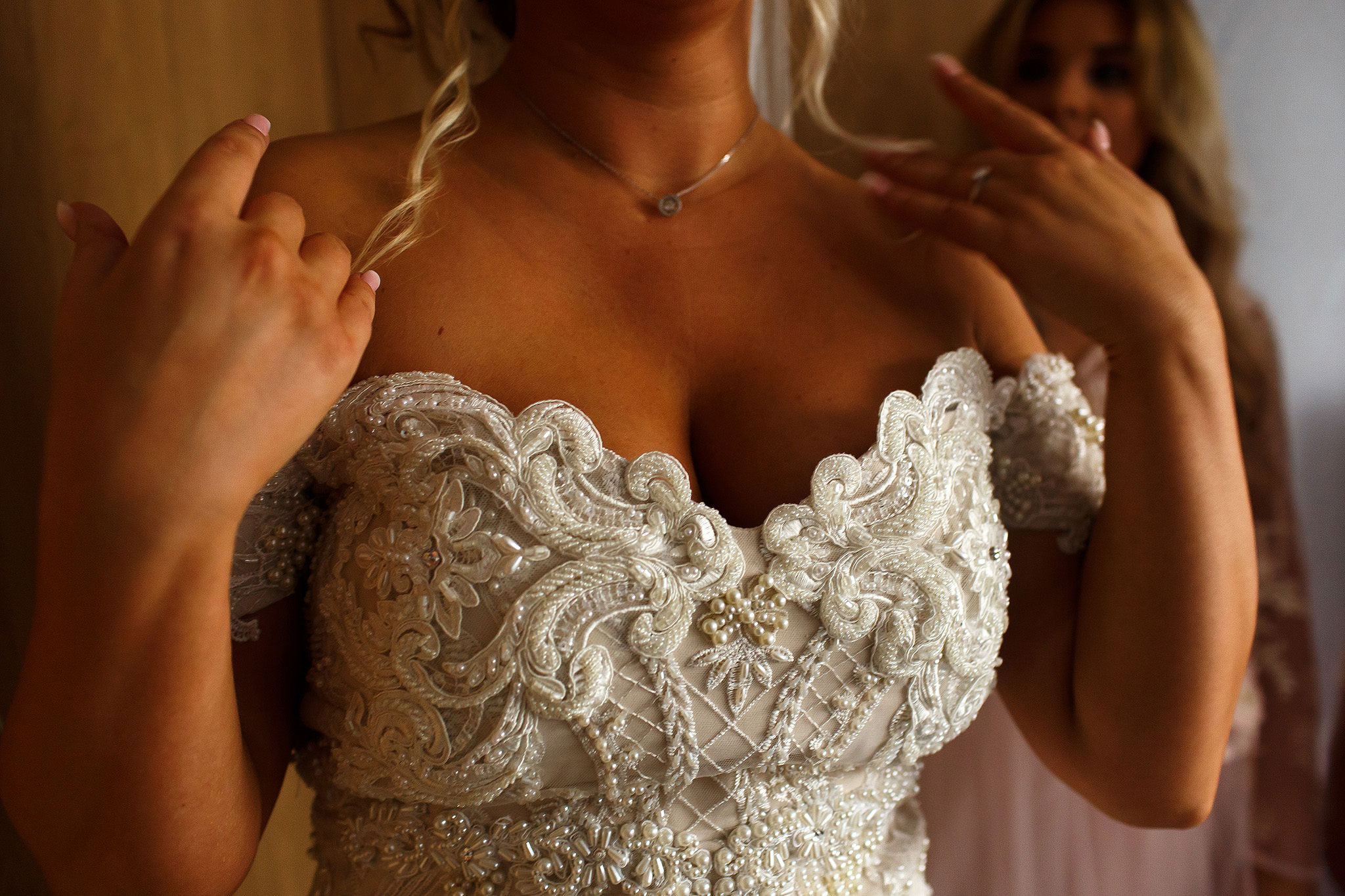 Bride wearing strapless wedding dress with beading, touching her blonde hair with hands