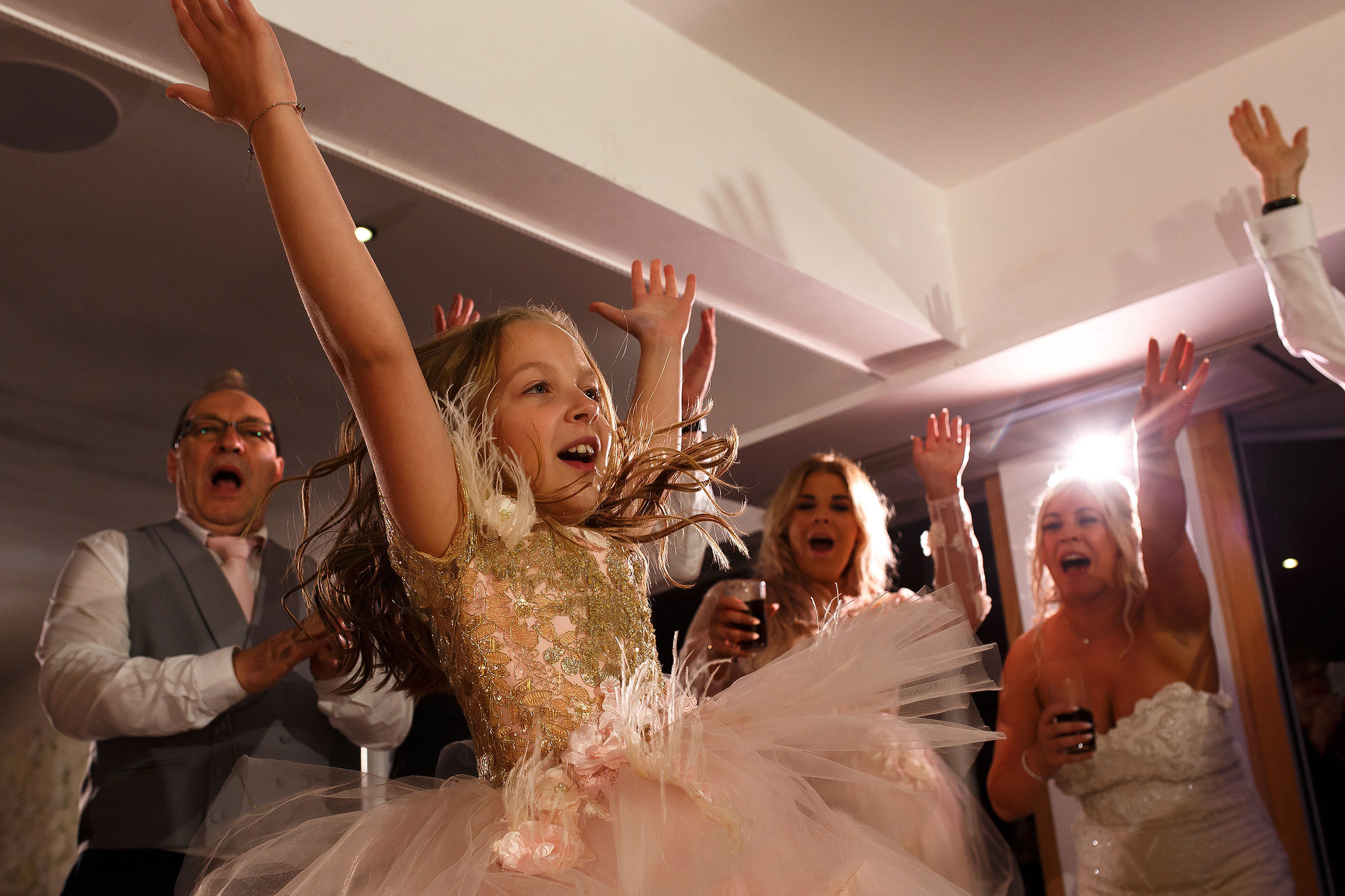 Flower girl throwing hands in the air on the wedding dance floor 