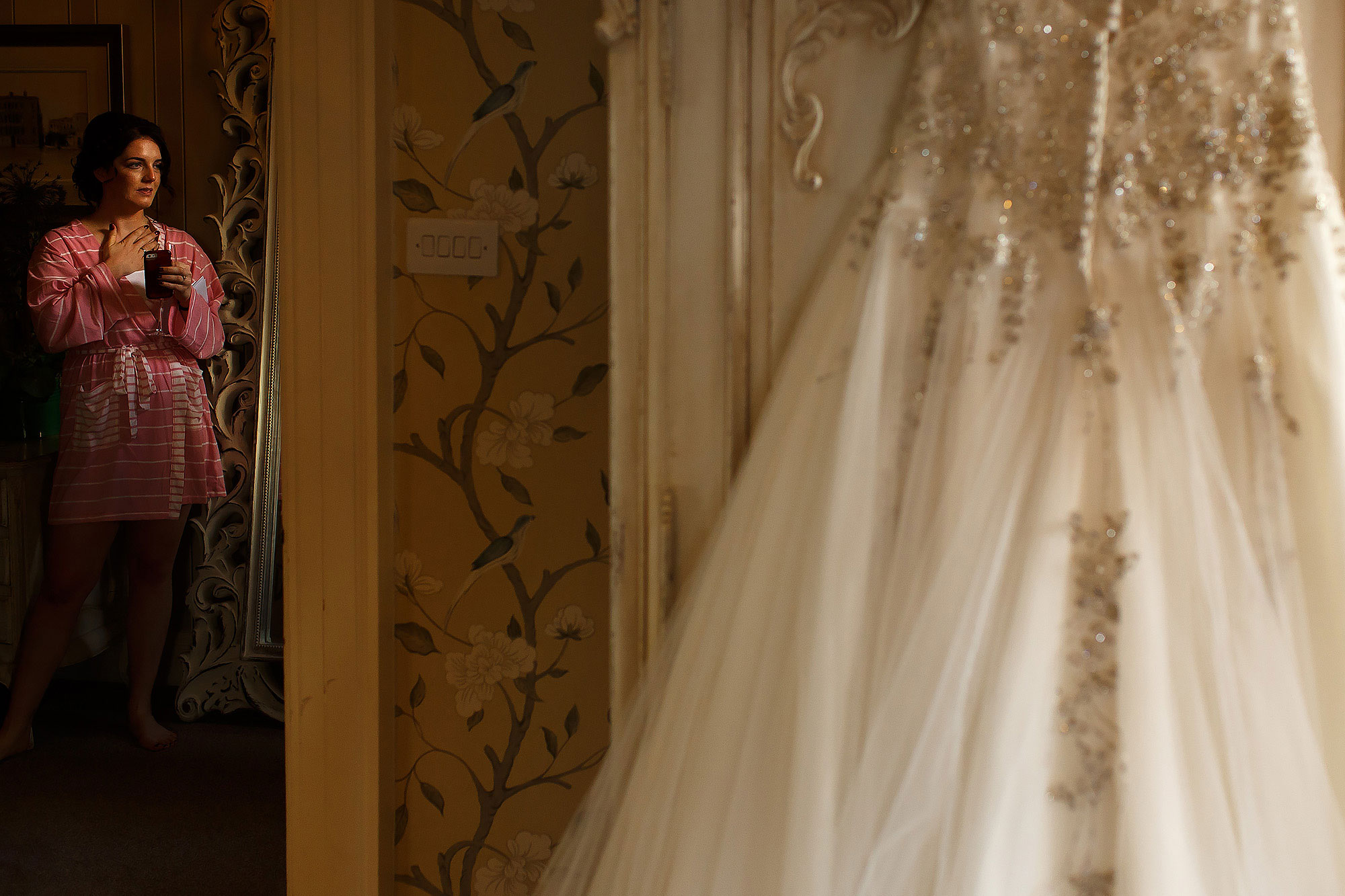 Bride holding hand to heart as she looks towards her wedding dress | Eaves Hall wedding photography by Toni Darcy