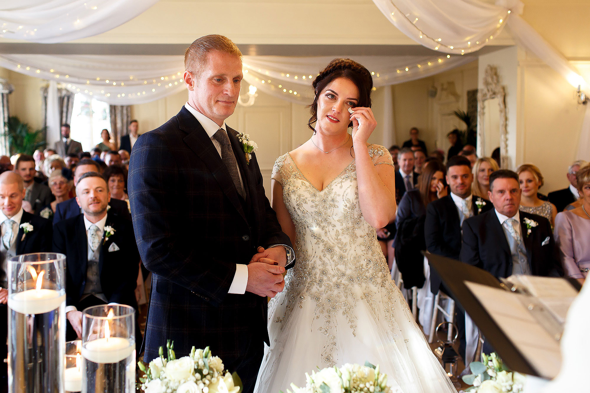 Bride and groom stood at the front looking tearful during wedding ceremony | Eaves Hall wedding photography by Toni Darcy