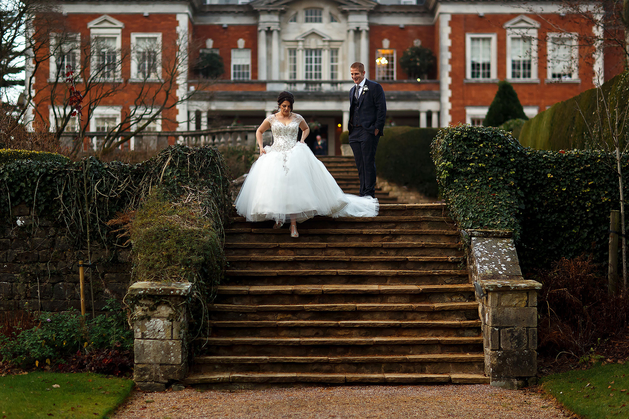 Bride walking into the gardens holding her dress as she walks down the steps with Eaves Hall in the background | Eaves Hall wedding photography by Toni Darcy