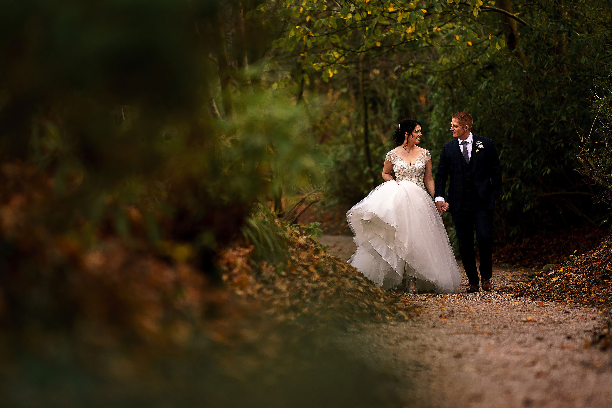 Bride and groom walking down the path way through the trees hand in hand | Eaves Hall wedding photography by Toni Darcy