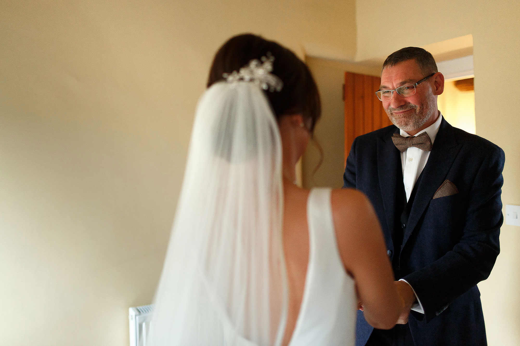 Bride wearing veil holding hands of her father as he sees her in her wedding dress for the first time.