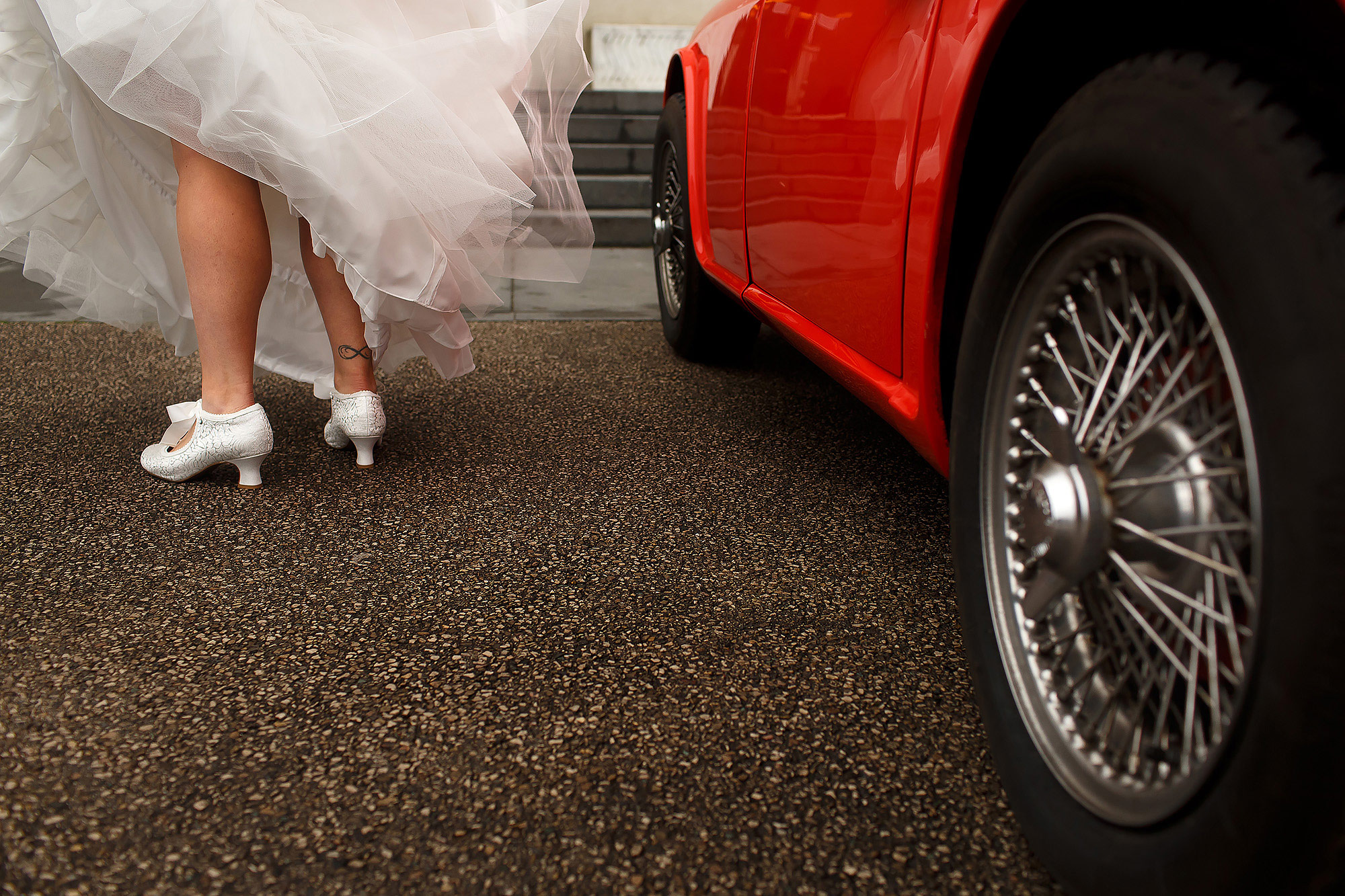 Bride stepping out of red vintage wedding car lifting her dress showing shoes at Leeds Civic Hall