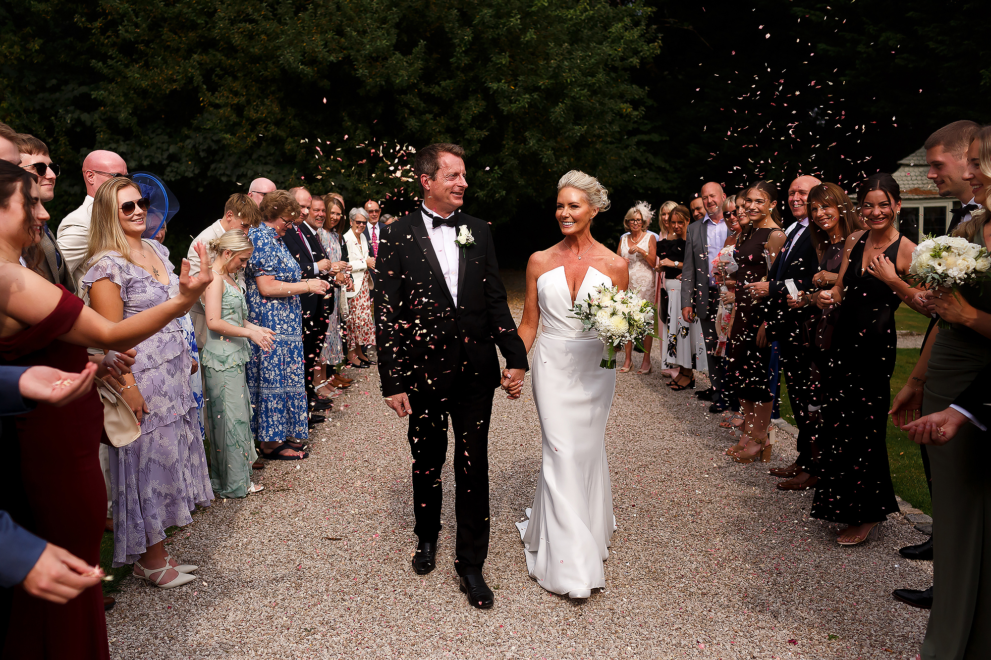 Bride with short blonde hair and groom wearing black tie suit walking through guests as they throw confetti at Bartle Hall